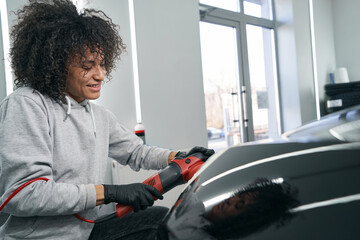 Joyous service station worker polishing auto with electric buffer