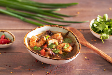 hot delicious asian seafood soup (shrimp, mussels, squid, shellfish) on a wooden background