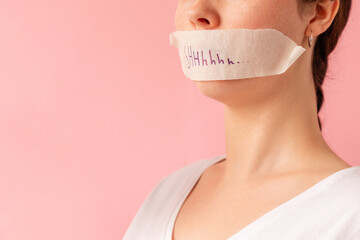 Portrait of a Caucasian woman with her mouth taped shut. Tape has the inscription Shhh. Pink...