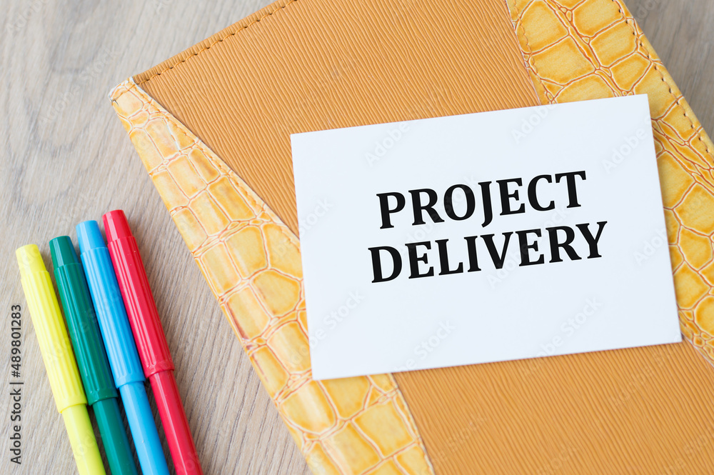 Aufkleber text project delivery on a card against the background of a yellow notebook on a wooden table