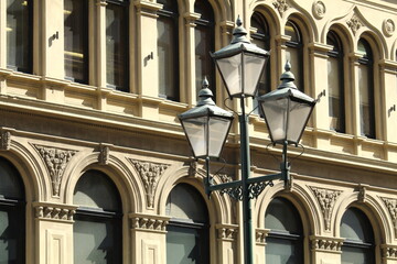A Victorian style street light with three lamps, with a heritage building in the background. Taken...