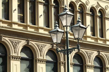 A Victorian style street light with three lamps, with a heritage building in the background. Taken in Dunedin, New Zealand, known for its art deco and gothic revival historical architecture.  © Zenobia Southcombe