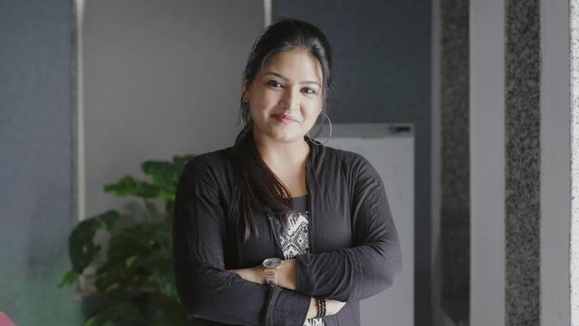 Smiling confident young pretty Indian woman looking at camera standing at office home in apartment arms crossed.Portrait of young successful business girl standing in office.
