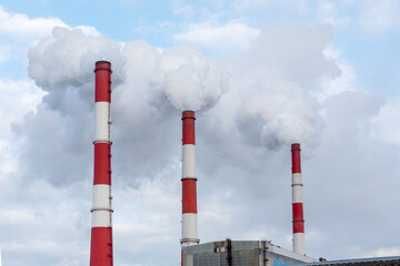 Three pipes of a thermal power plant with steam and smoke against a blue sky during the heating season