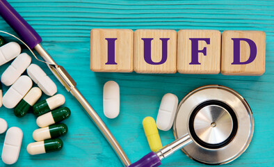 IUFD - acronym on wooden cubes on a blue background with a stethoscope and tablets