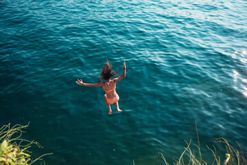 Woman jumping off cliff into the sea. Summer fun lifestyle.