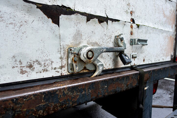 Angled close up view of a rusted metal latch on the back of a white moving truck, with a black step ladder attached