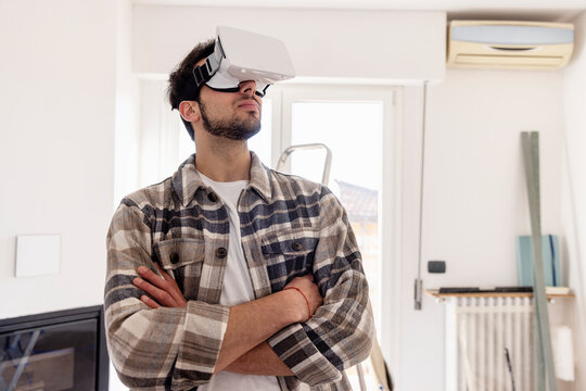 Young man with arms crossed wearing VR glasses in new living room