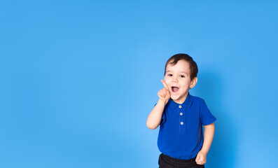 Portrait of a happy little boy on a blue background with thumbs up - The concept of childhood, growing up and achievements - front view, space for text