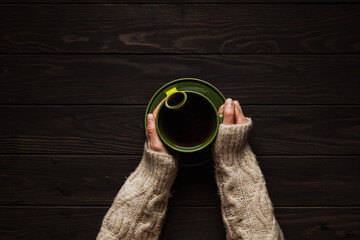 Woman in a cozy beige sweater holding a big cup of hot tea in hands on wooden background, overhead shot, copy space