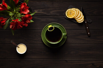 A big cup of hot tea, sliced lemon, honey, knife and flowers on wooden background, overhead shot