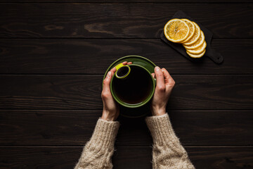 Woman in a cozy beige sweater holding a big cup of hot tea in hands on wooden background, overhead shot, copy space