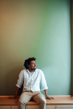 Smiling man listening music through headphones at home
