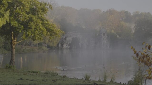 Grotto behind misty clouds at Majolan Park lake in Blanquefort France, Slow dolly right shot