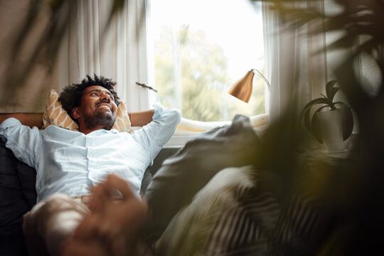 Happy Man With Hands Behind Head Resting On Sofa At Home