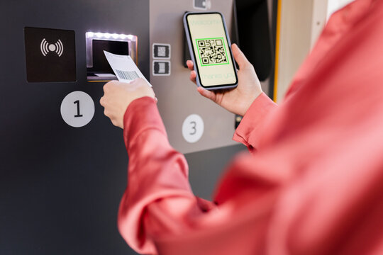 Woman scanning QR code on ticket machine through smart phone at station