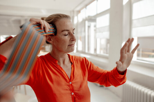 Businesswoman with eyes closed touching computer cables to head and gesturing in office