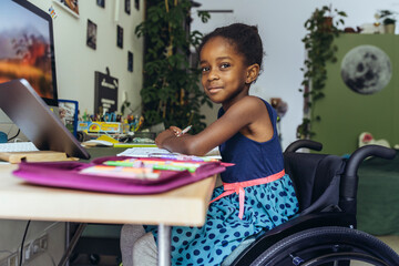 Smiling girl sitting on wheelchair and studying at home