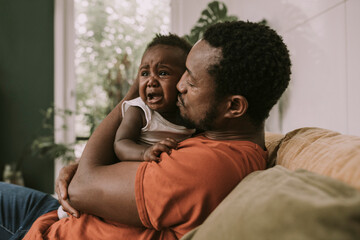 Father calming down baby boy crying in living room