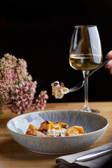 pumpkin with stracciatella and microgreen on wooden table. Woman hold fork with pumpkin and glass of white wine on background
