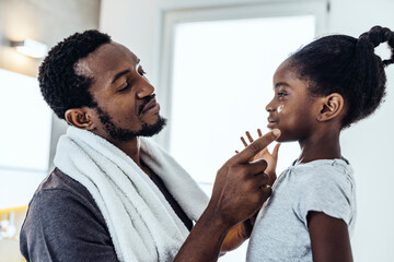 Father applying moisturizer to daughter in bathroom