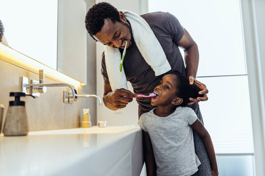 Father brushing teeth of daughter in bathroom at home
