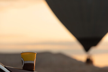 A cup of morning coffee against a blurred magic view with hot air balloon in the sky during...