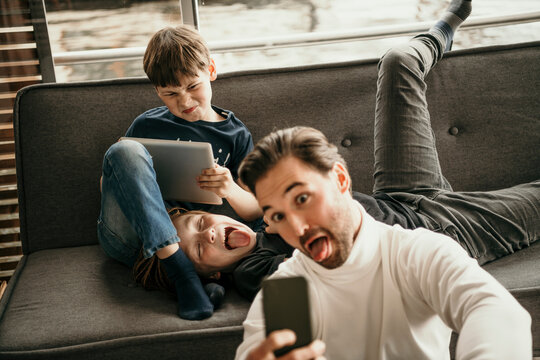 Man sticking out tongue taking selfie with sons making faces at home