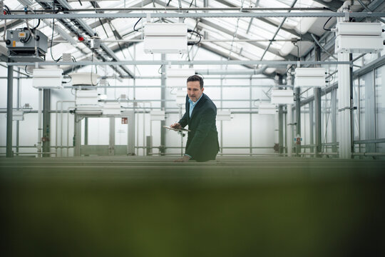 Businessman holding tablet PC analyzing machinery in greenhouse