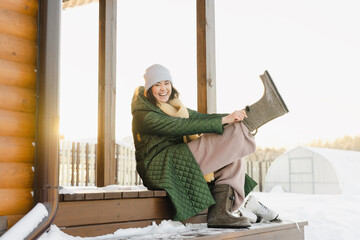 Happy woman wearing boots sitting at porch of house in snowy garden