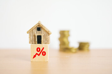 miniature house on down percent icon on wood cube and blurred stack of coins on wooden desk , for...