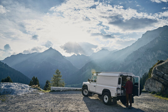 Tourist standing by off-road vehicle on sunny day, Graubunden Canton, Maloja Pass, Switzerland