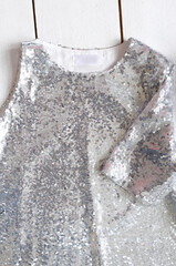 Silver sequin fabric dress with one sleeve for girl on white wooden background. White blank...