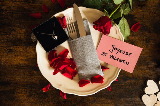 vue du dessus d'une assiette rempli de pétale de rose rouge avec écrit en Français joyeuse saint valentin et un bijou 