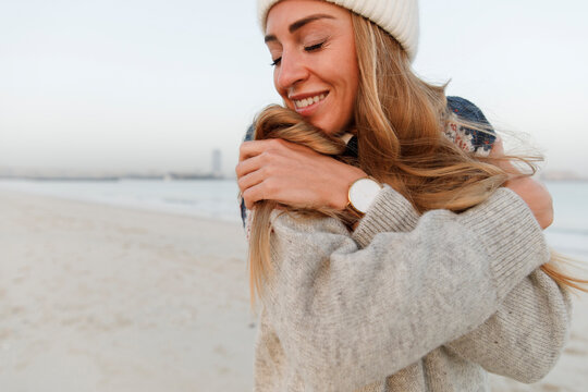 Happy woman with eyes closed hugging self at beach