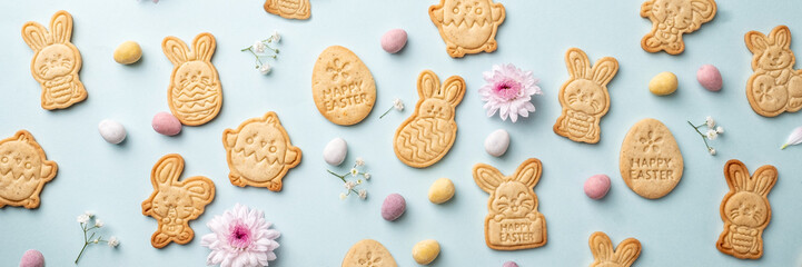 Bunny shaped sugar cookies with Easter chocolate eggs and flower background. Happy Easter