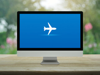 Airplane flat icon on desktop modern computer monitor screen on wooden table over blur pink flower and tree in park,  Business airplane transportation online concept