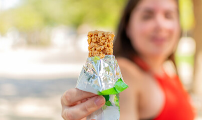 Close up of woman holding a cereal bar ready to eat in spring in a park.