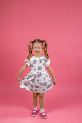 a little girl in a beautiful dress with curly tails on a solid pink background