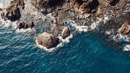 Aerial top view of waves break on rocks in a blue ocean. Sea waves on beautiful beach aerial view...