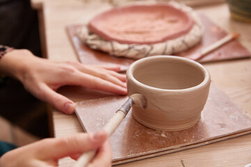 faceless woman paints a clay bowl. close up