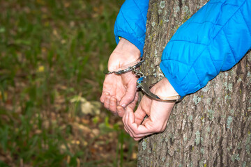 The girl is tied to a tree with handcuffs. Violence.