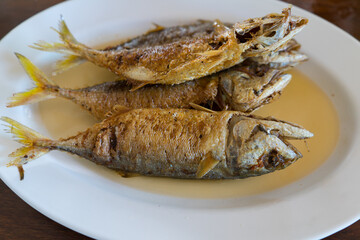Fried mackeral fish  with  sour sauce for health food on white plate. Delicious Thai food on wooden table background.