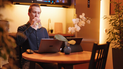 Man working on laptop computer in kitchen stay hydrated with bottle of water