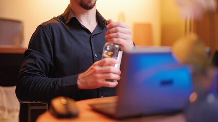 Headless person behind the laptop computer drink water from glass bottle