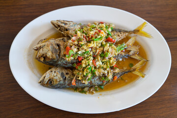 Fried mackeral fish  with chlli sauce with sweet and sour sauce and topping with coriander,red chili, garlic and herb vegetables spicy on topping.Delicious Thai food on wooden wooden table background.
