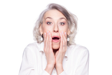 Portrait of a modern mature woman looking at camera with open mouth and hands at her face scared, surprised and shocked isolated on white background