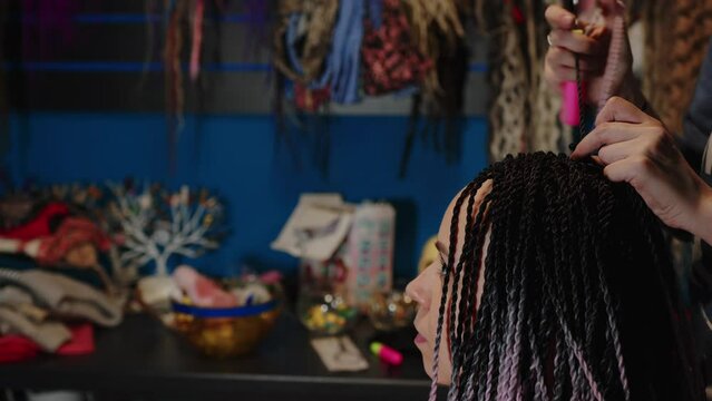 A female stylist attaches Senegalese braids to a woman in a beauty salon. Portrait of a beautiful lady with Senegalese pigtails in casual clothes. A hipster girl gets her hair done