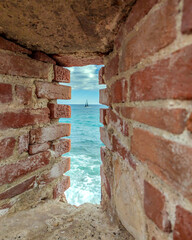Voiler sur la mer méditerranée au travers d'une meurtrière dans les remparts d'Antibes sur la Côte d'Azur - obrazy, fototapety, plakaty