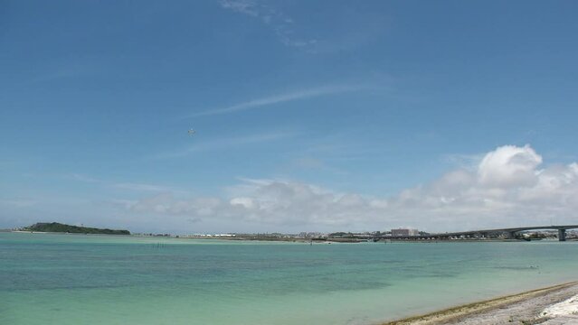 TOMIGUSUKU, OKINAWA, JAPAN - AUGUST 2021 : View of Senaga island beach (Ocean or sea) and airplane in daytime. Clear blue summer sky and clouds. Holiday, vacation and resort concept video.